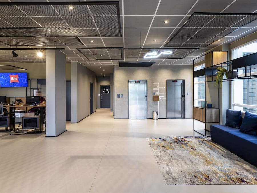 Un espacio de oficina moderno con área de recepción, una pantalla de televisión, escritorios, computadoras y un sofá con alfombra.