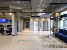 Um espaço de escritório moderno com área de recepção, tela de TV, mesas, computadores e um sofá com tapete.