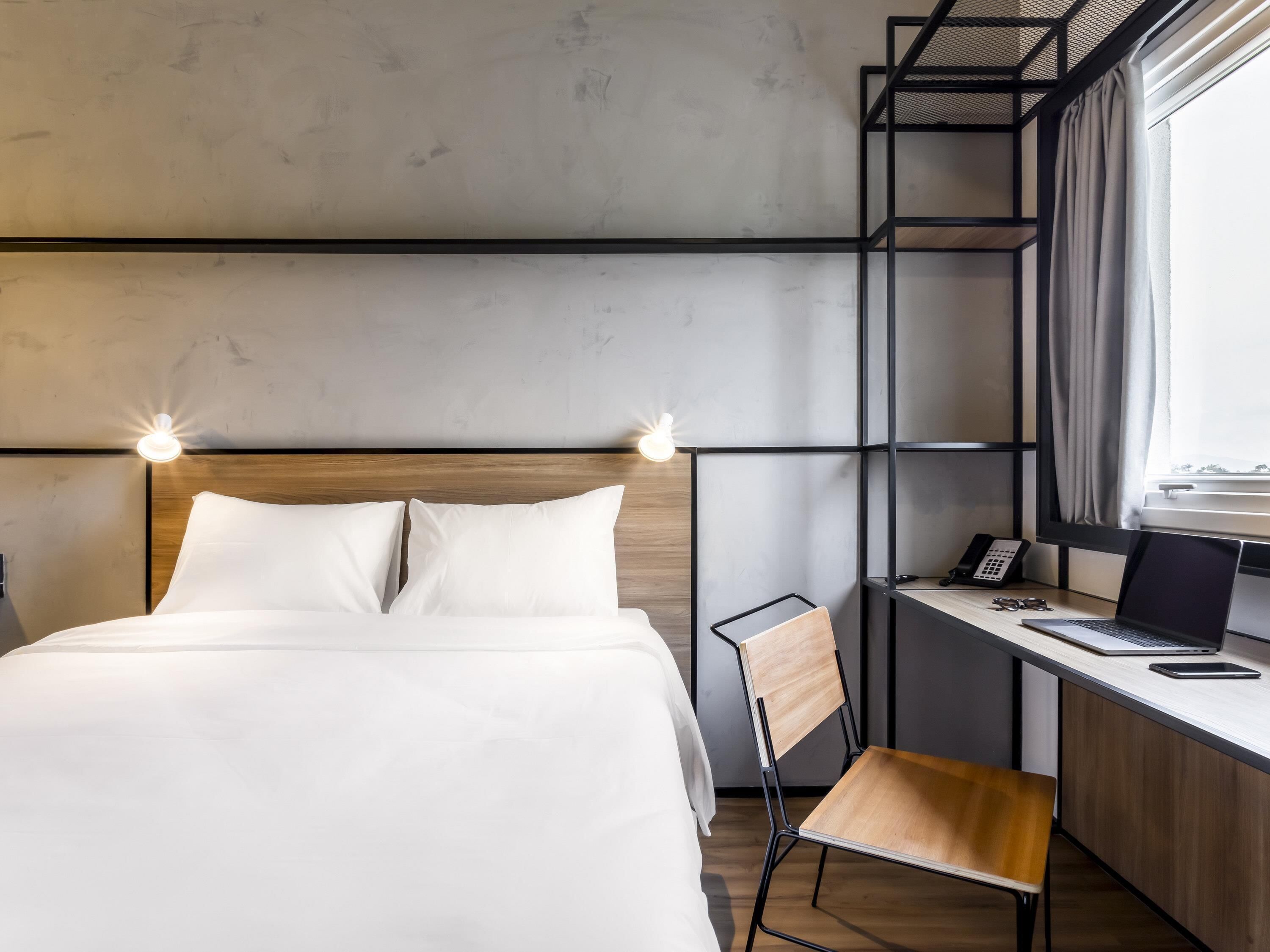 Une chambre d’hôtel moderne équipée d’un lit, d’un bureau, d’une chaise et offrant une vue sur l’extérieur.
