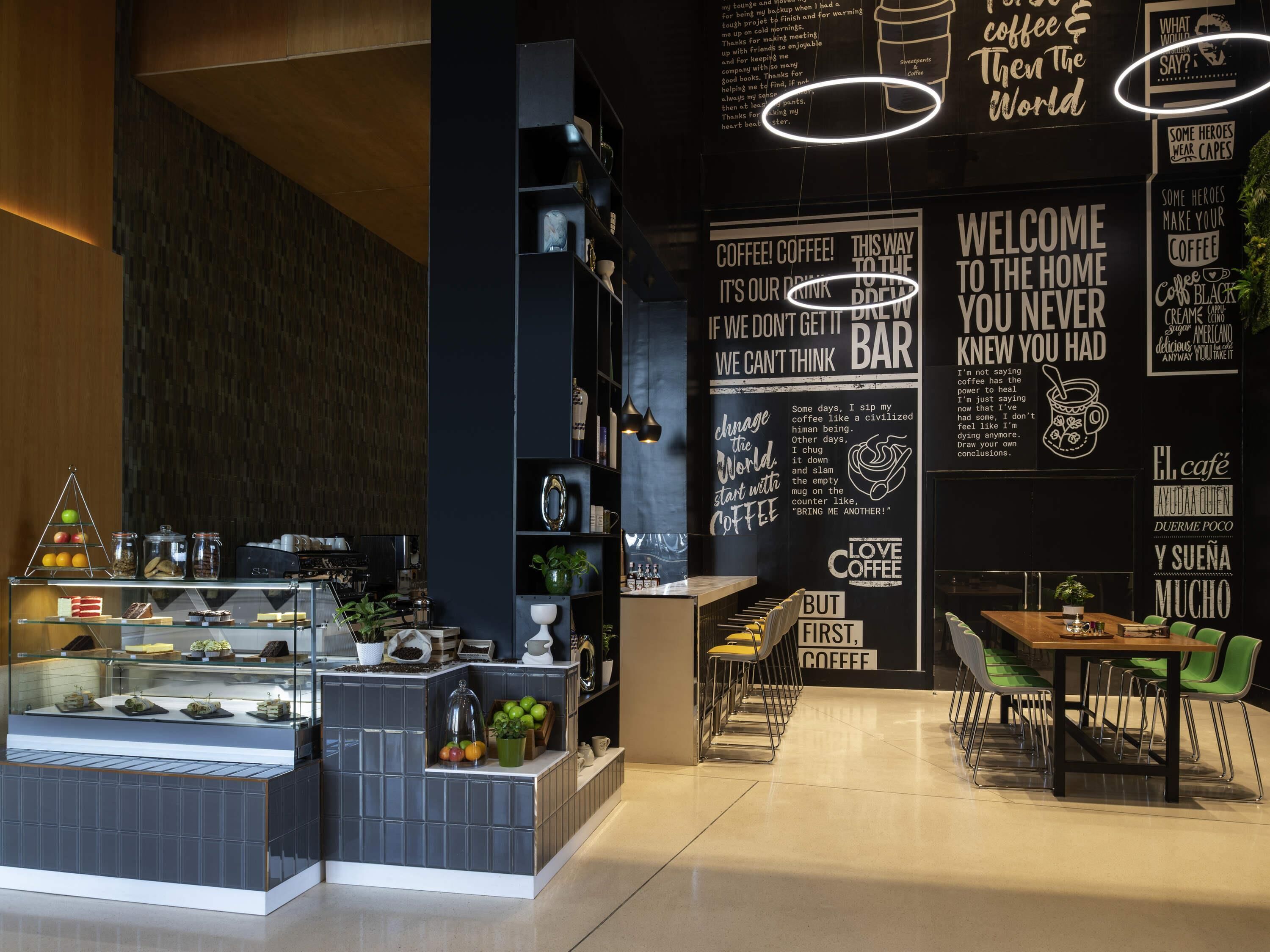 Un café moderno con una pared de pizarra que muestra diversas citas motivacionales y una vitrina de vidrio con pasteles.