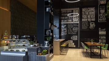 Un café moderno con una pared de pizarra que muestra diversas citas motivacionales y una vitrina de vidrio con pasteles.