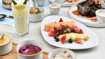 Uma mesa com diversos pratos, incluindo uma salada de frutas, um copo de bebida amarela e várias pequenas tigelas de comida.