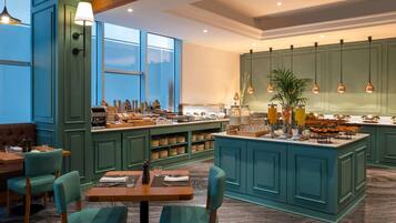 A modern kitchen with teal cabinetry, a central island with breakfast items, and a seating area with a wooden table and teal chairs.