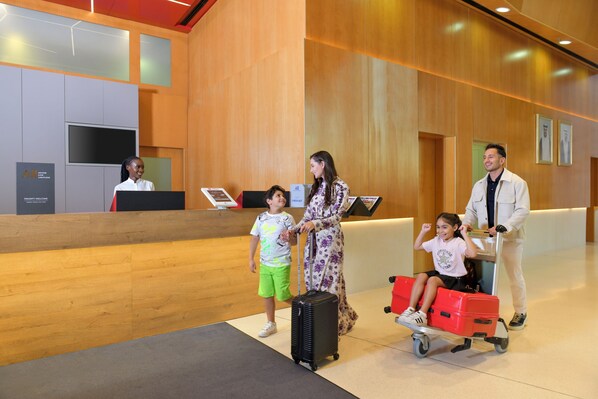A reception area with a wooden reception desk, a TV screen, and a wall-mounted sign. - Ibis Doha (Doha)