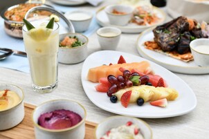 Una mesa con diversos platos, incluyendo una bandeja de frutas, un vaso de una bebida amarilla y varios cuencos pequeños de comida.
