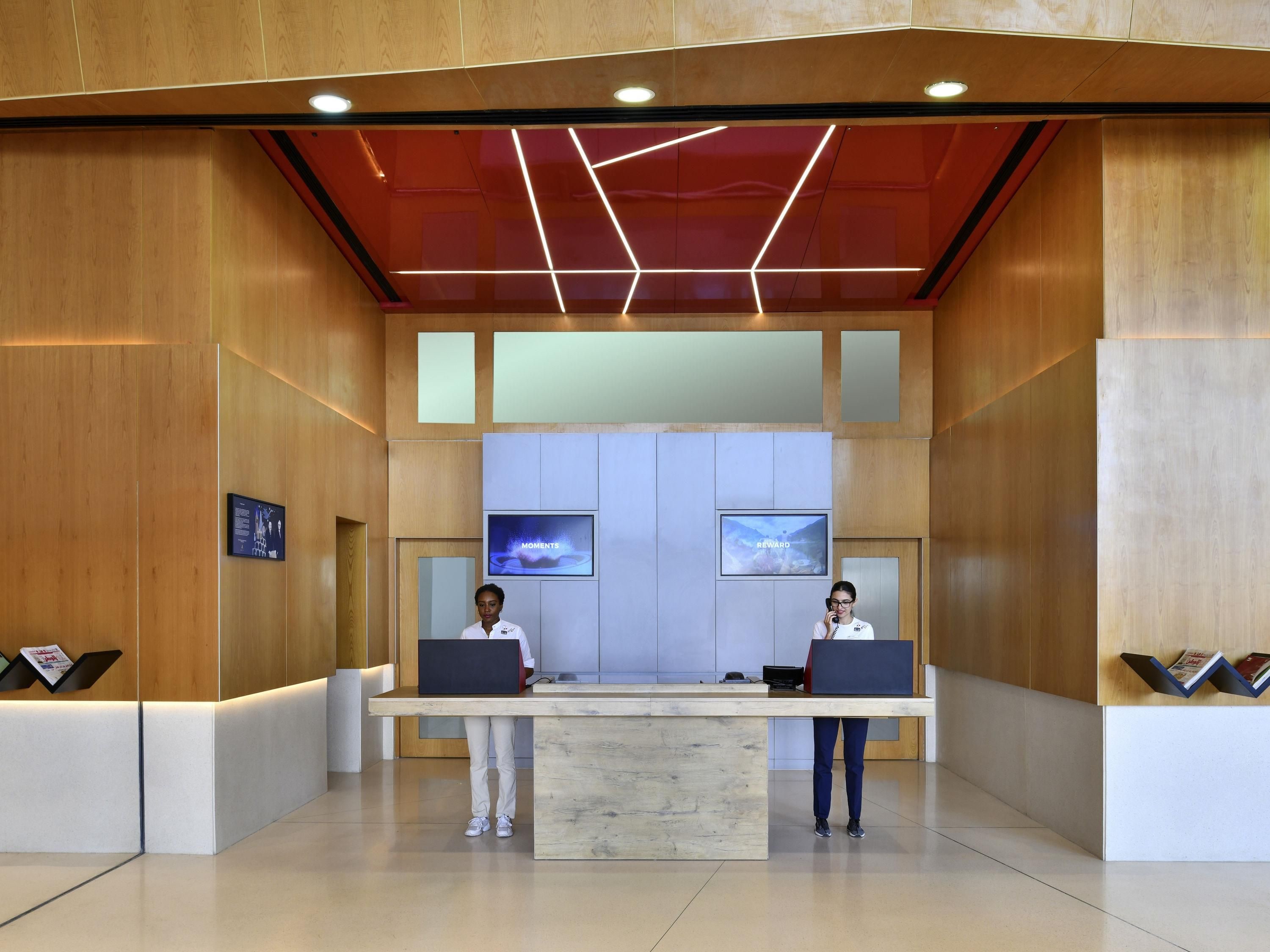 Tauleller de recepció amb dos empleats, un disseny interior modern i dos monitors que mostren contingut.