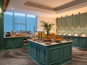 A spacious kitchen with teal cabinetry, a central island with food items, and pendant lighting. - Ibis Doha (Doha)