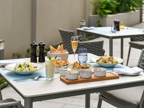 An outdoor dining area with tables set for meals, including salads, bread, and drinks. - Ibis Doha (Doha)