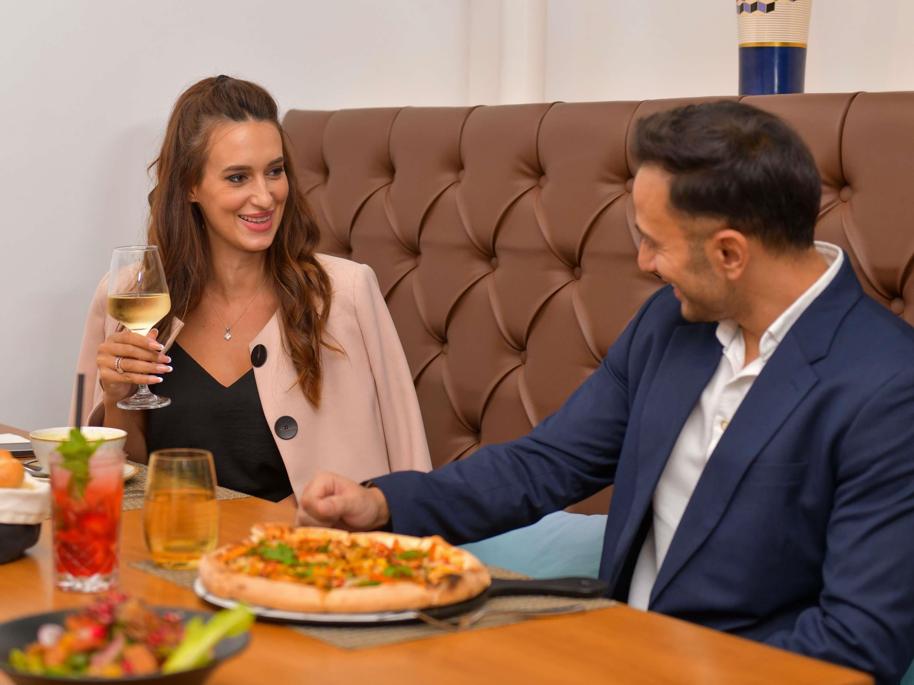 A dining table with a pizza, a glass of wine, and a salad.