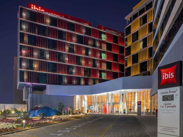 A modern hotel with a prominent red and yellow facade, large windows, and a well-lit entrance area.