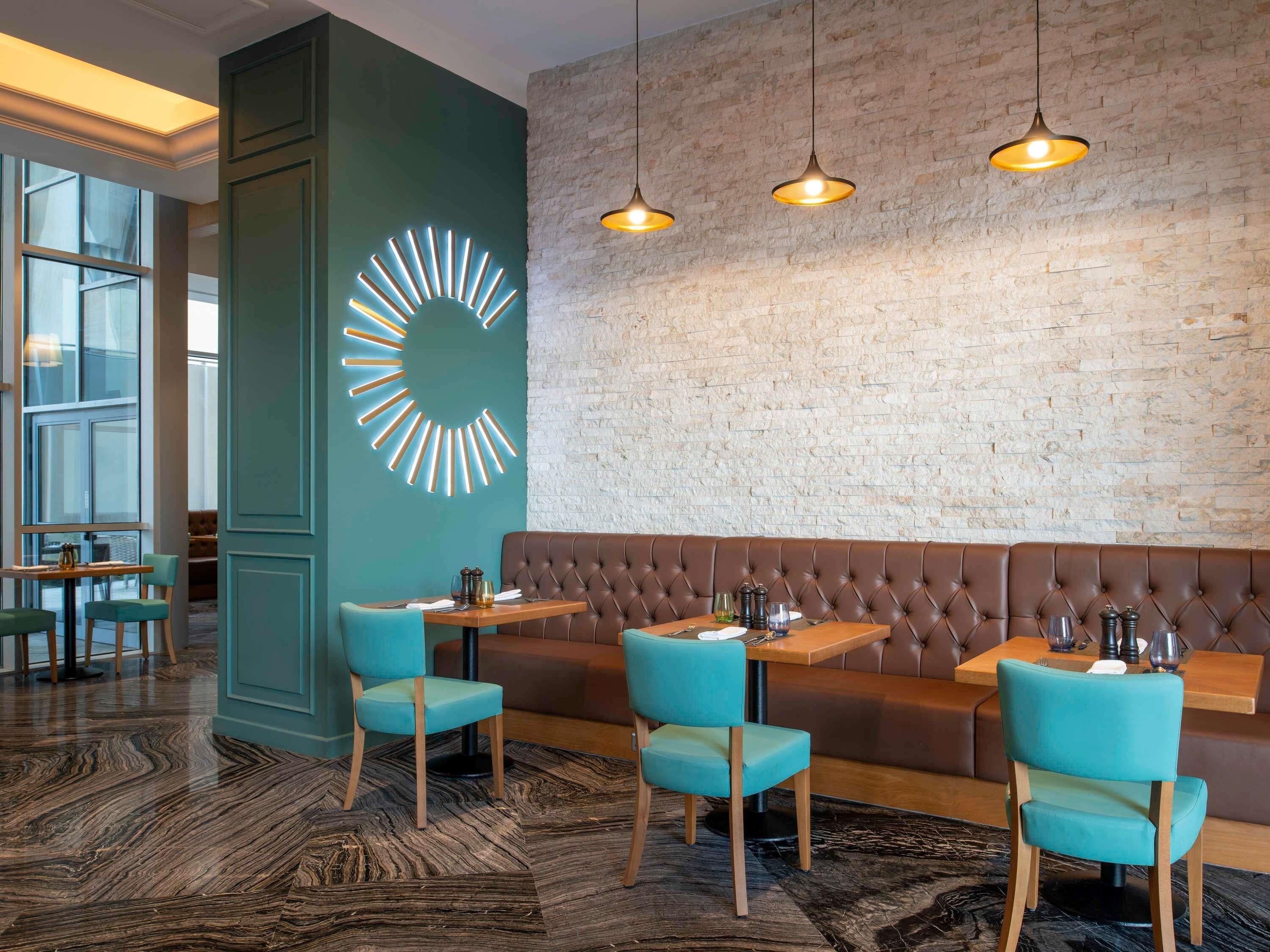 Un restaurante con pared de ladrillo, lámpara moderna y un banco con capitoné.
