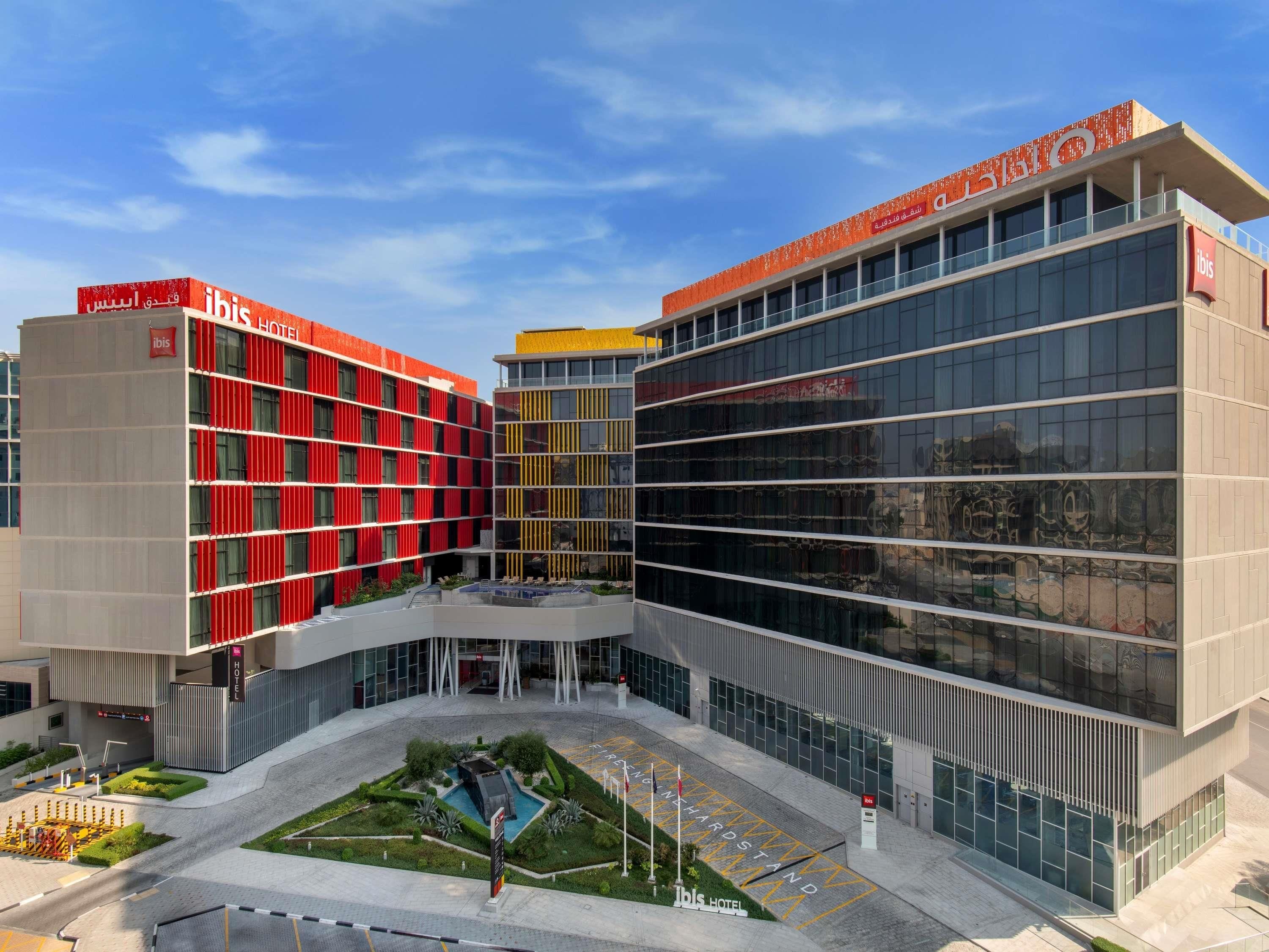 A modern hotel with a red facade, a glass entrance, and a landscaped courtyard.