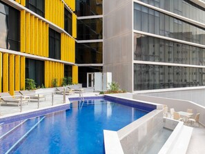 A modern indoor pool with clear blue water, yellow vertical panels, and a seating area with chairs and a table. - Ibis Doha (Doha)