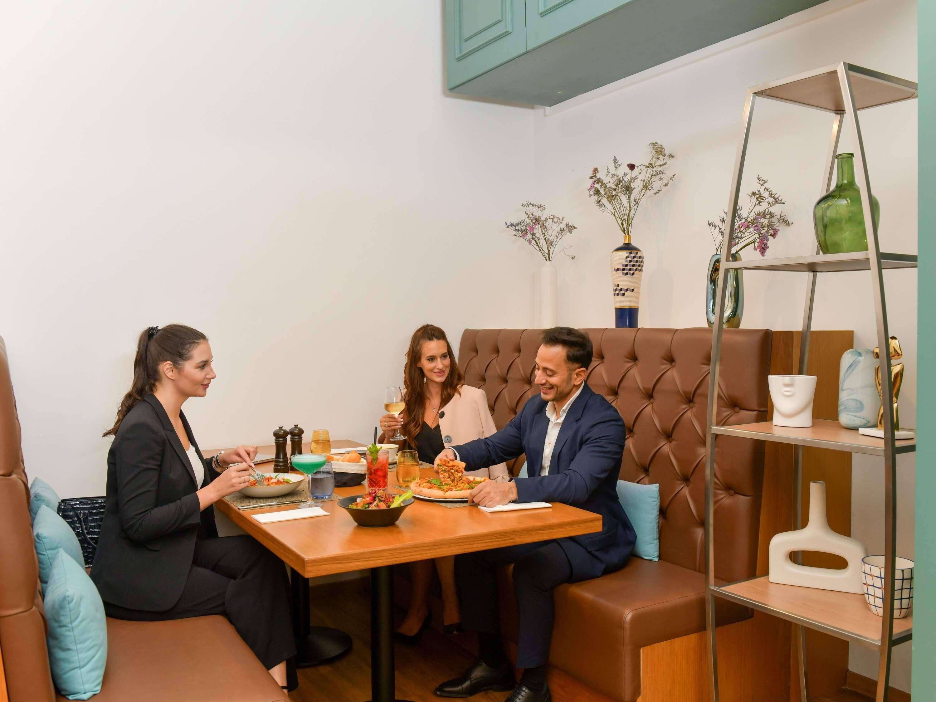 A dining area with a wooden table, brown cushioned seating, and a metal shelf with decorative items.