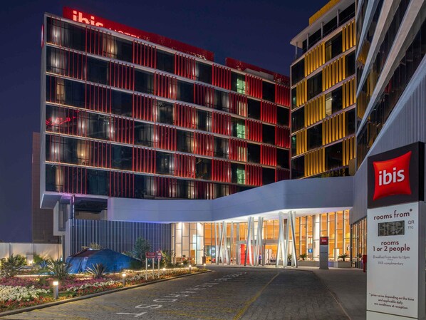 A modern hotel with a prominent red and yellow facade, large windows, and a well-lit entrance area. - Ibis Doha (Doha)