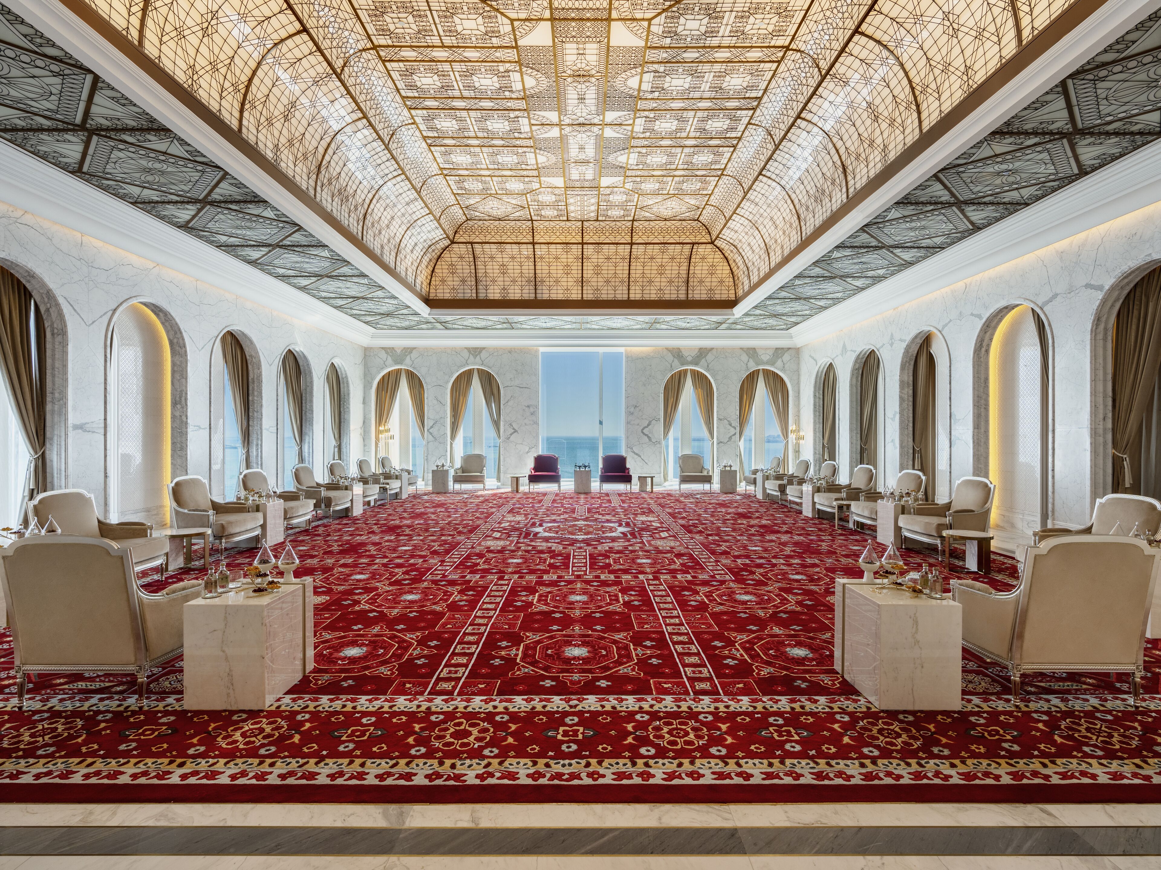 A luxurious hotel room with a large red carpet, marble walls, and a high ceiling with intricate designs.
