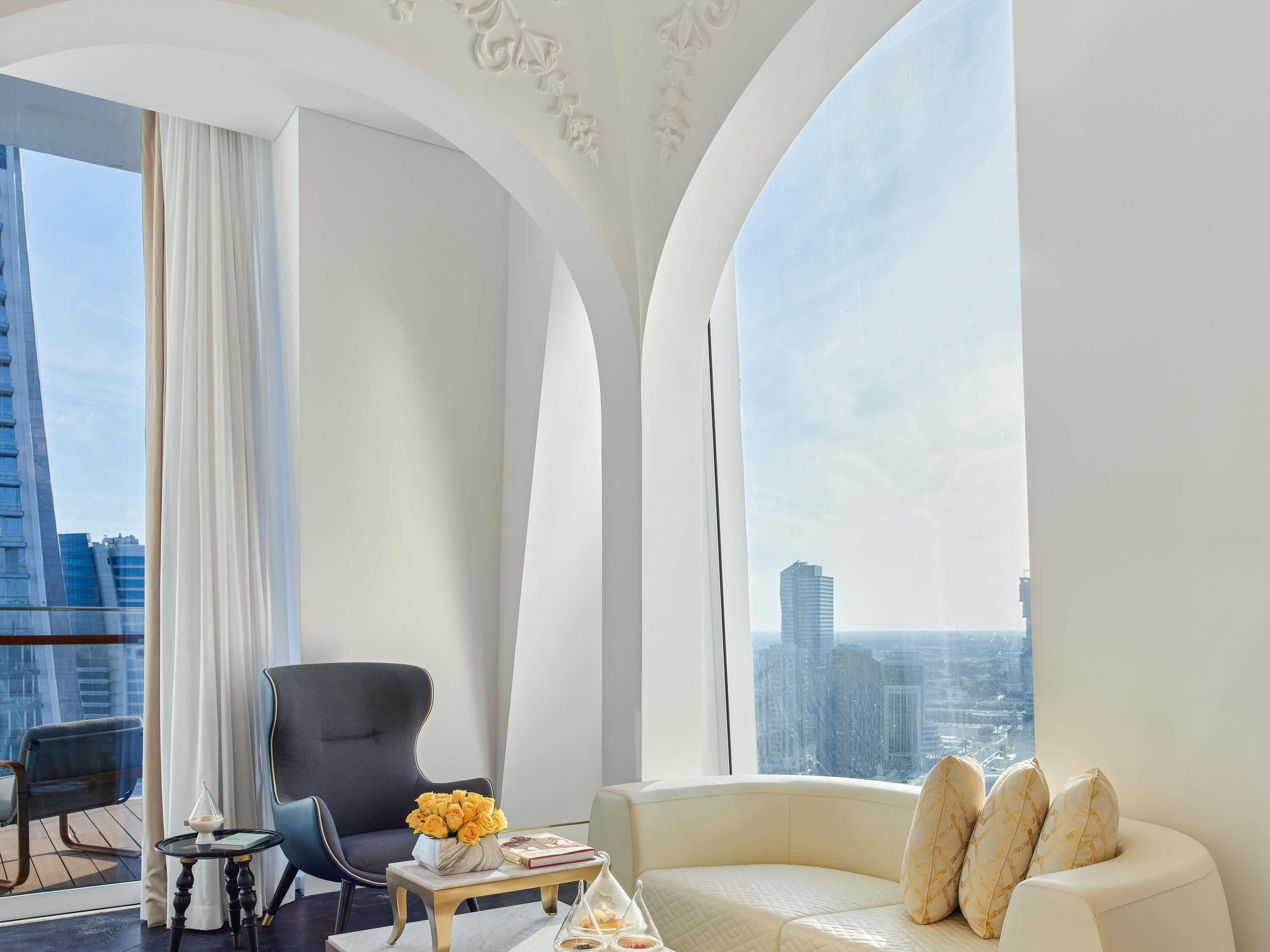 A modern hotel room with a curved sofa, a black armchair, and a small table with a vase of yellow flowers.