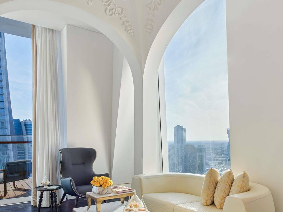 A modern hotel room with a curved sofa, a black armchair, and a small table with a vase of yellow flowers.