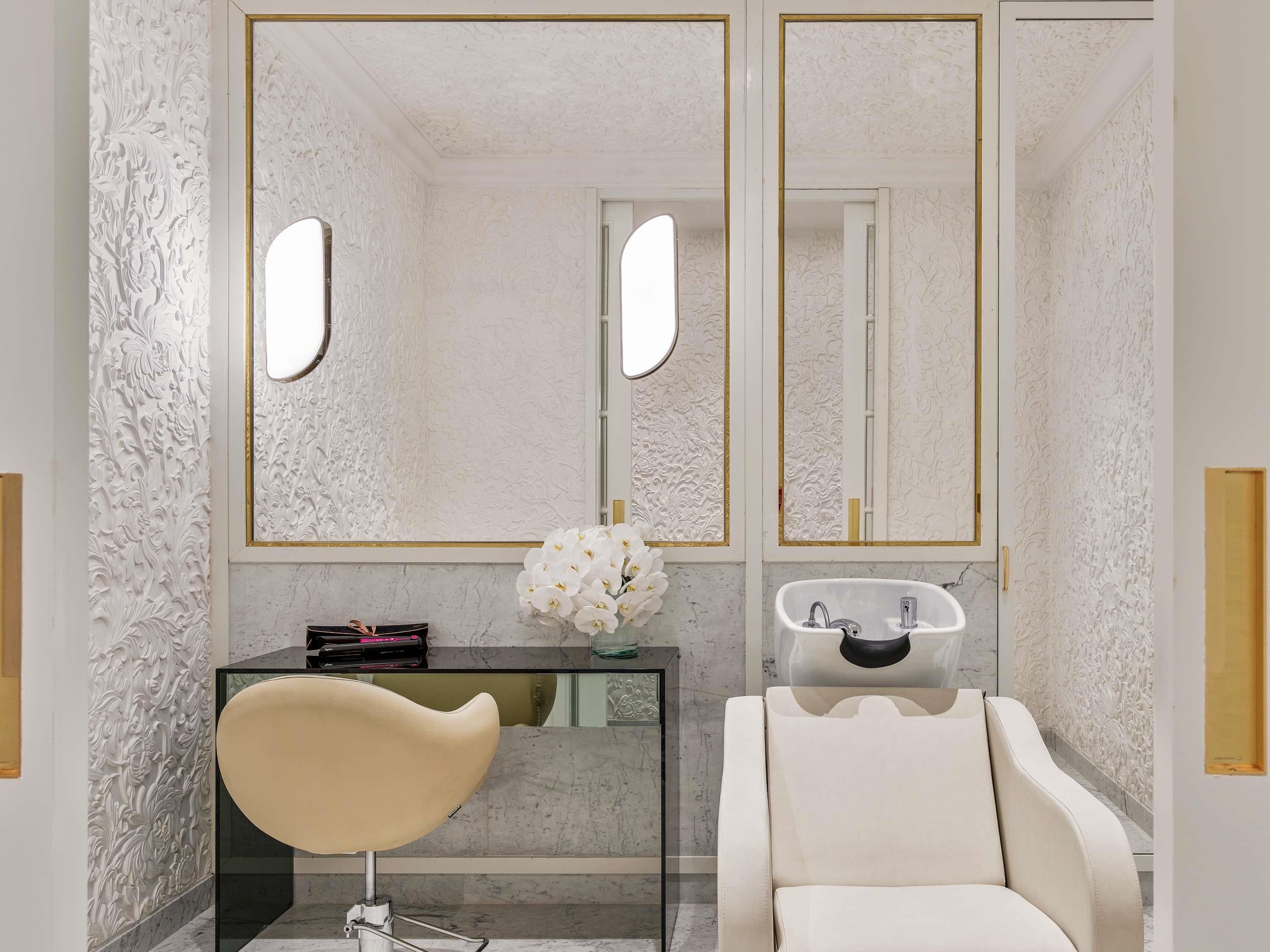 A bathroom with a marble countertop, a white chair, a vanity with a mirror, and a vase of white flowers.