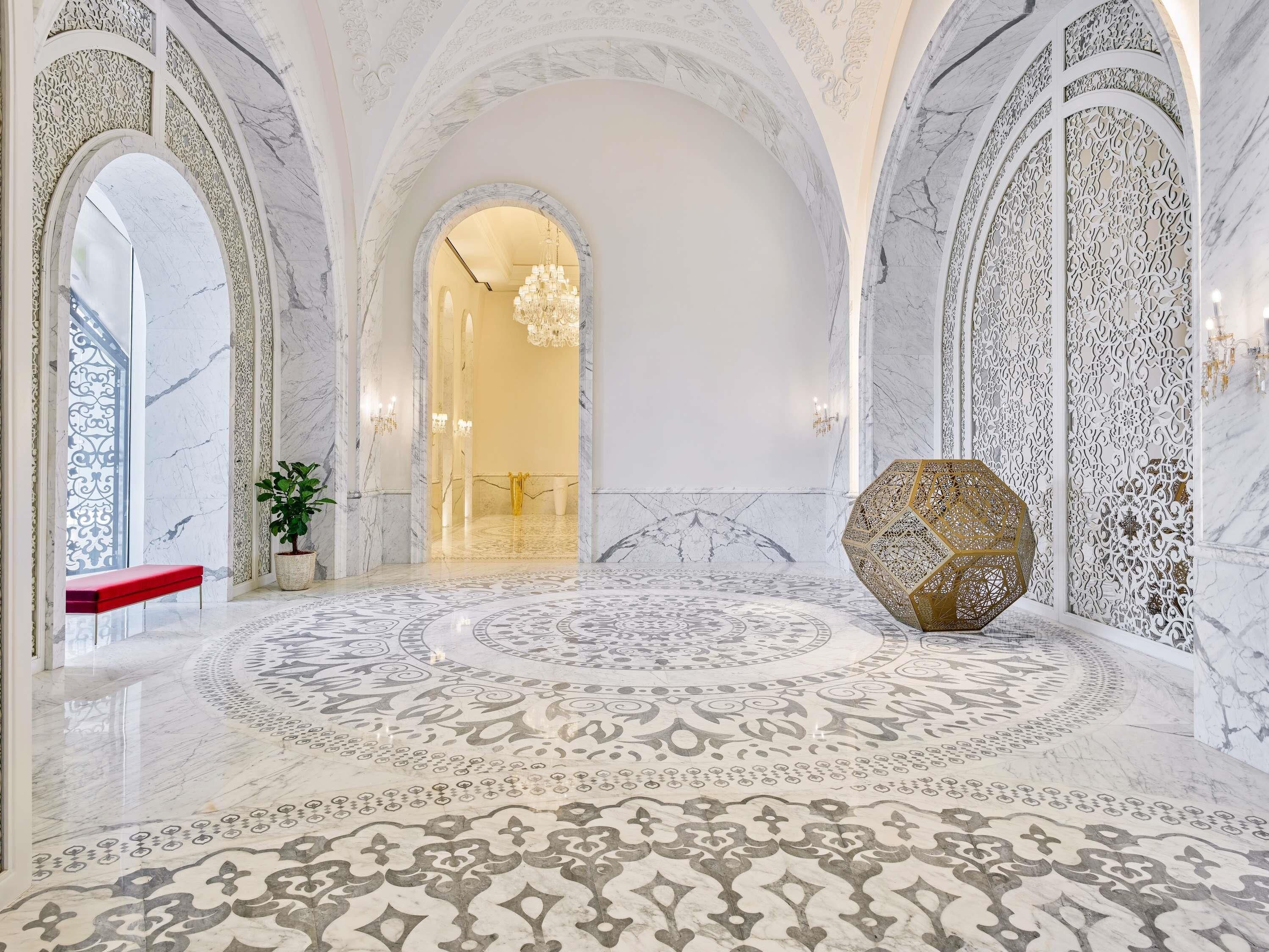 Interior com pisos de mármore, portas em arco e detalhes elaborados nas paredes.