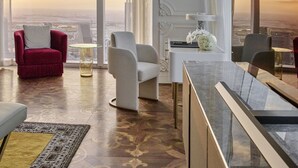 A spacious room with a large window offering a city view, a modern dining area, and a seating arrangement with a red chair and a white chair. - Raffles Doha (Doha)