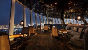 A high-rise interior with panoramic city views, modern furniture, and ambient lighting.