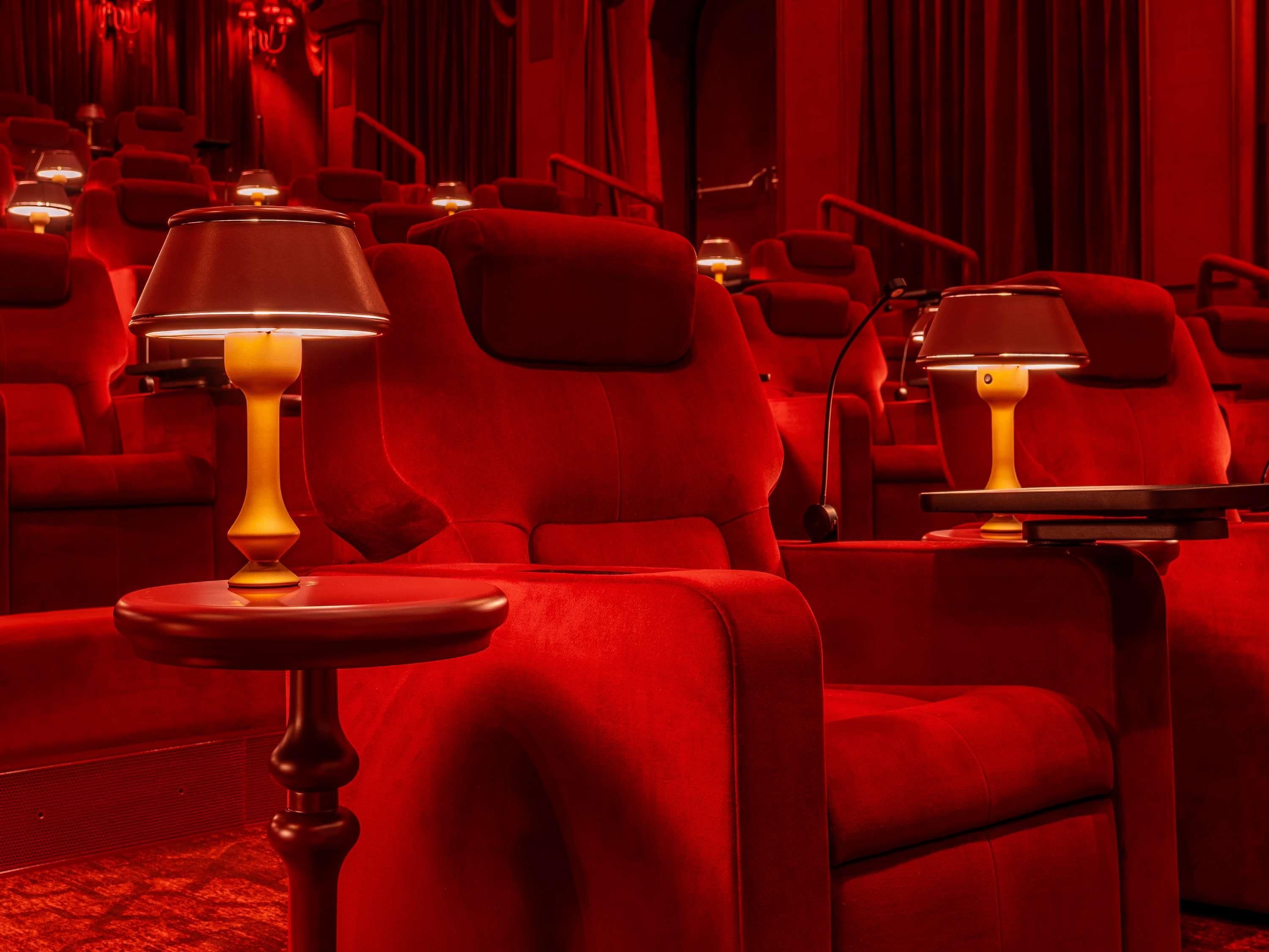 Un teatro con asientos rojos y mesas con lámparas.