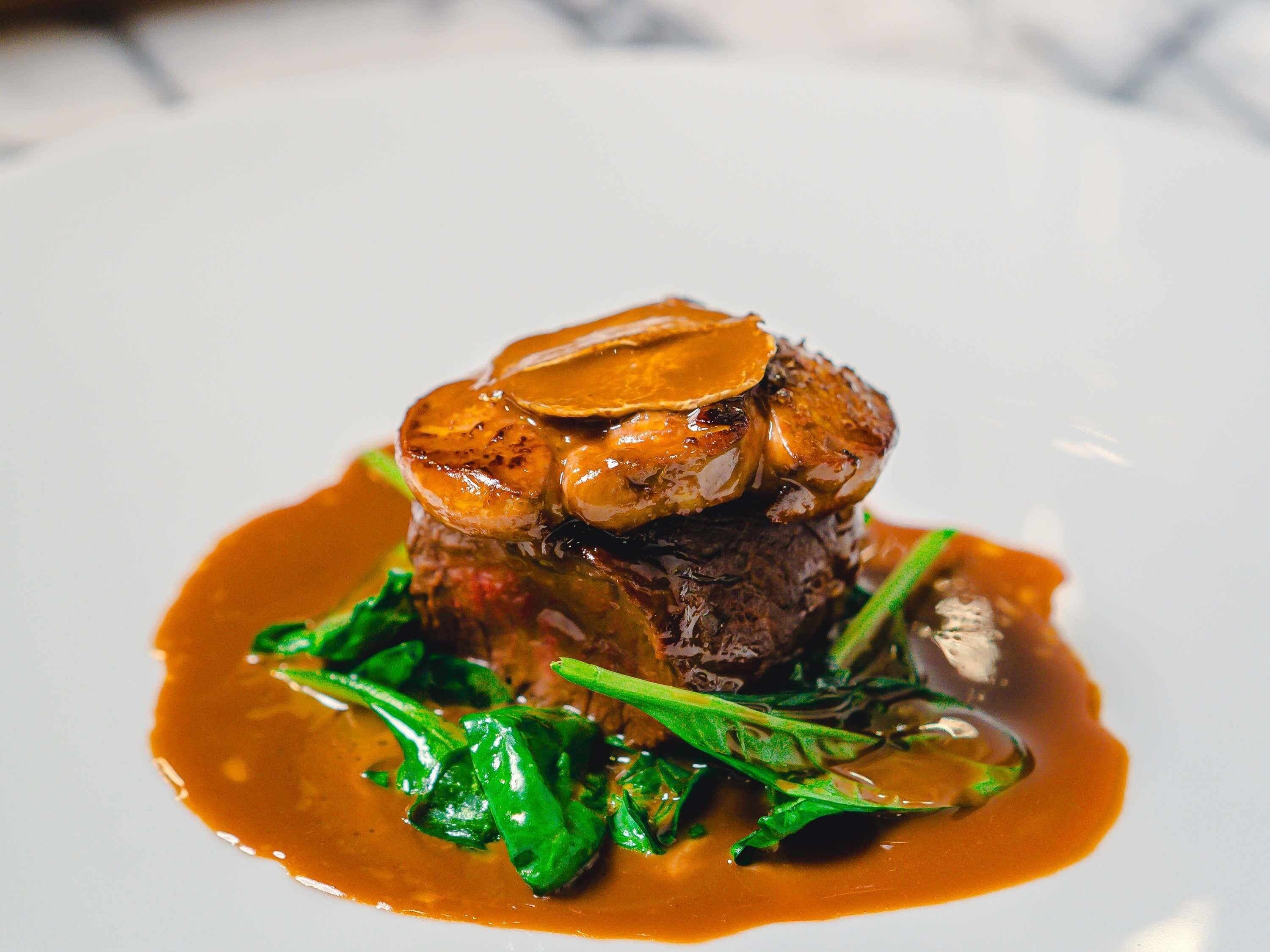 A plated dish with a steak, mushrooms, and greens.