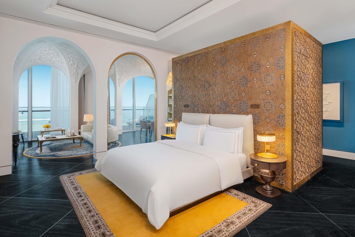 Una habitación de hotel moderna con una cama grande, un balcón con vistas y una decoración de pared.