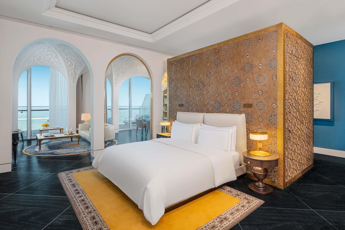 A modern hotel room with a large bed, a balcony with a view, and a decorative wall.