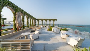 An outdoor seating area with white furniture and a view of the sea. - Raffles Doha (Doha)
