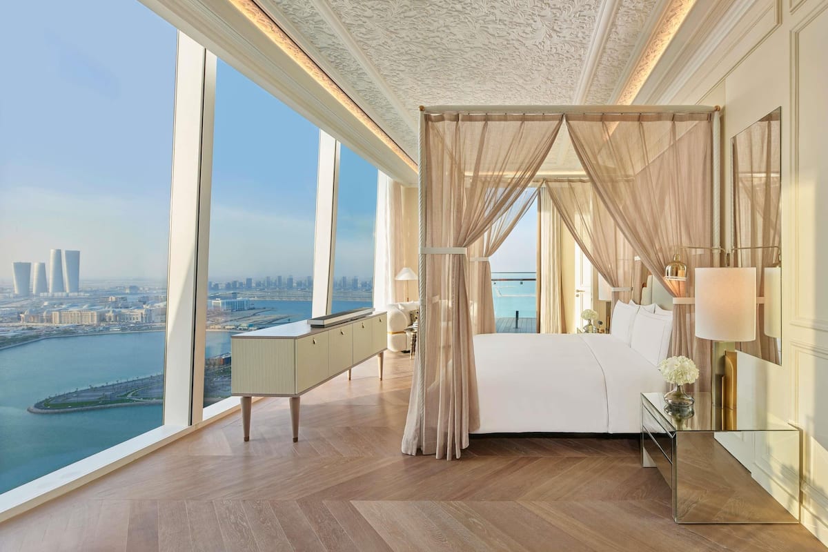 A high-rise bedroom with a city view, a large bed, a bedside table, and a nightstand.