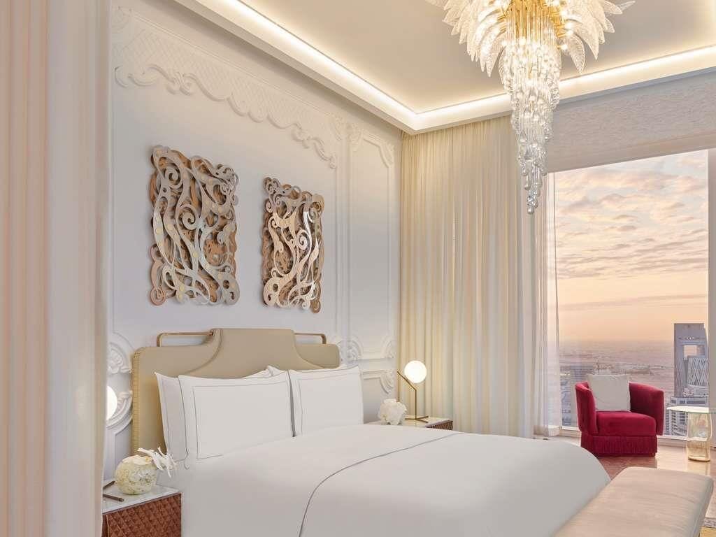 A modern hotel room with a large bed, decorative wall art, a chandelier, and a city view.