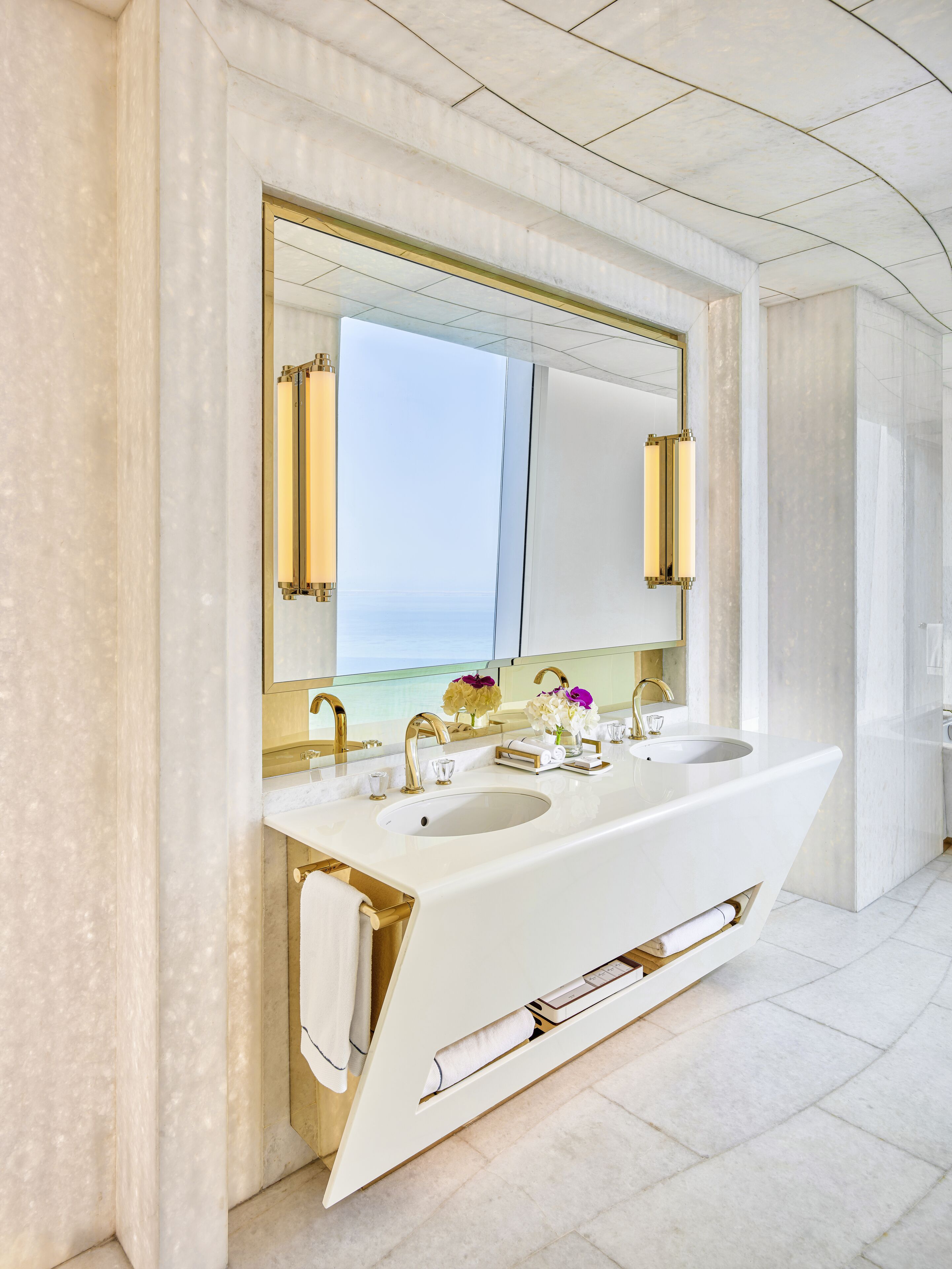 A modern bathroom with a large mirror, two sinks, and gold fixtures.