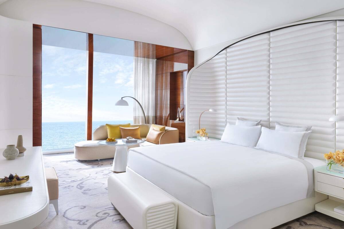 Quarto moderno com uma cama grande, um sofá, uma mesinha de apoio e vista para o mar.
