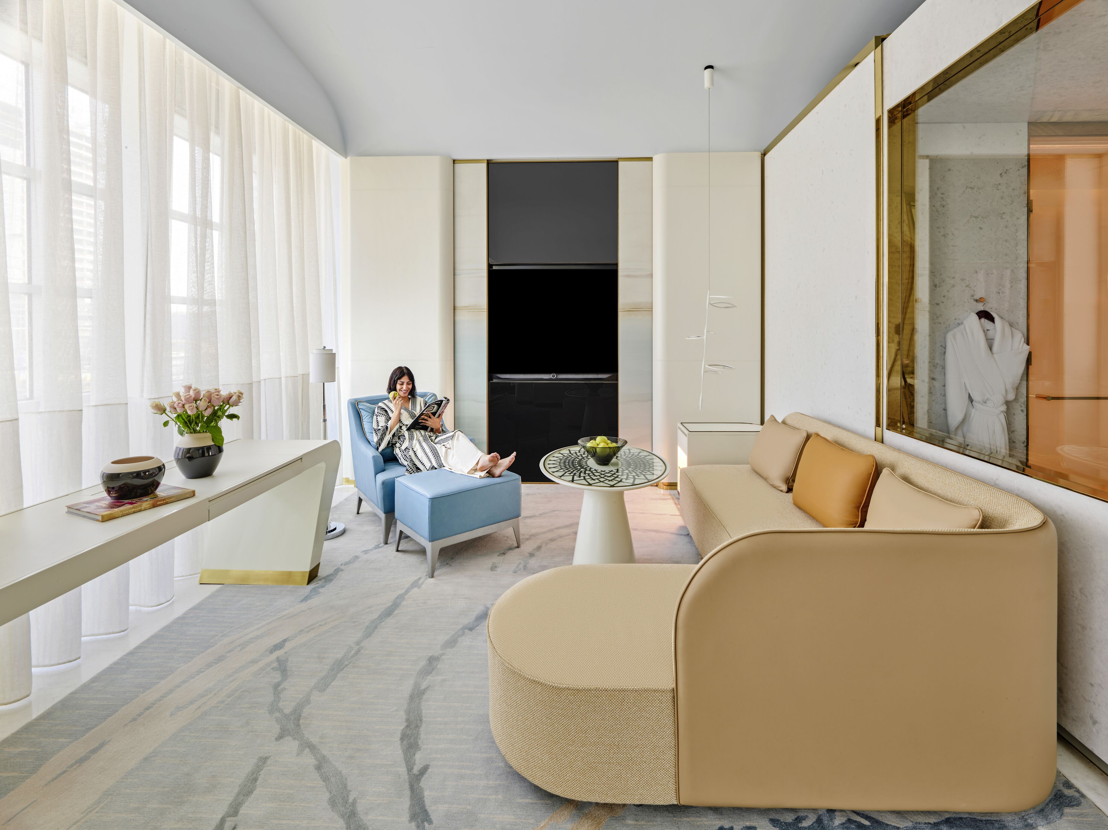 Uma sala de estar moderna com um sofá, uma poltrona azul, uma mesa de centro e uma televisão.