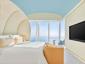 Una habitación de hotel moderna con una cama grande, una zona de estar y un ventanal con vistas al mar.