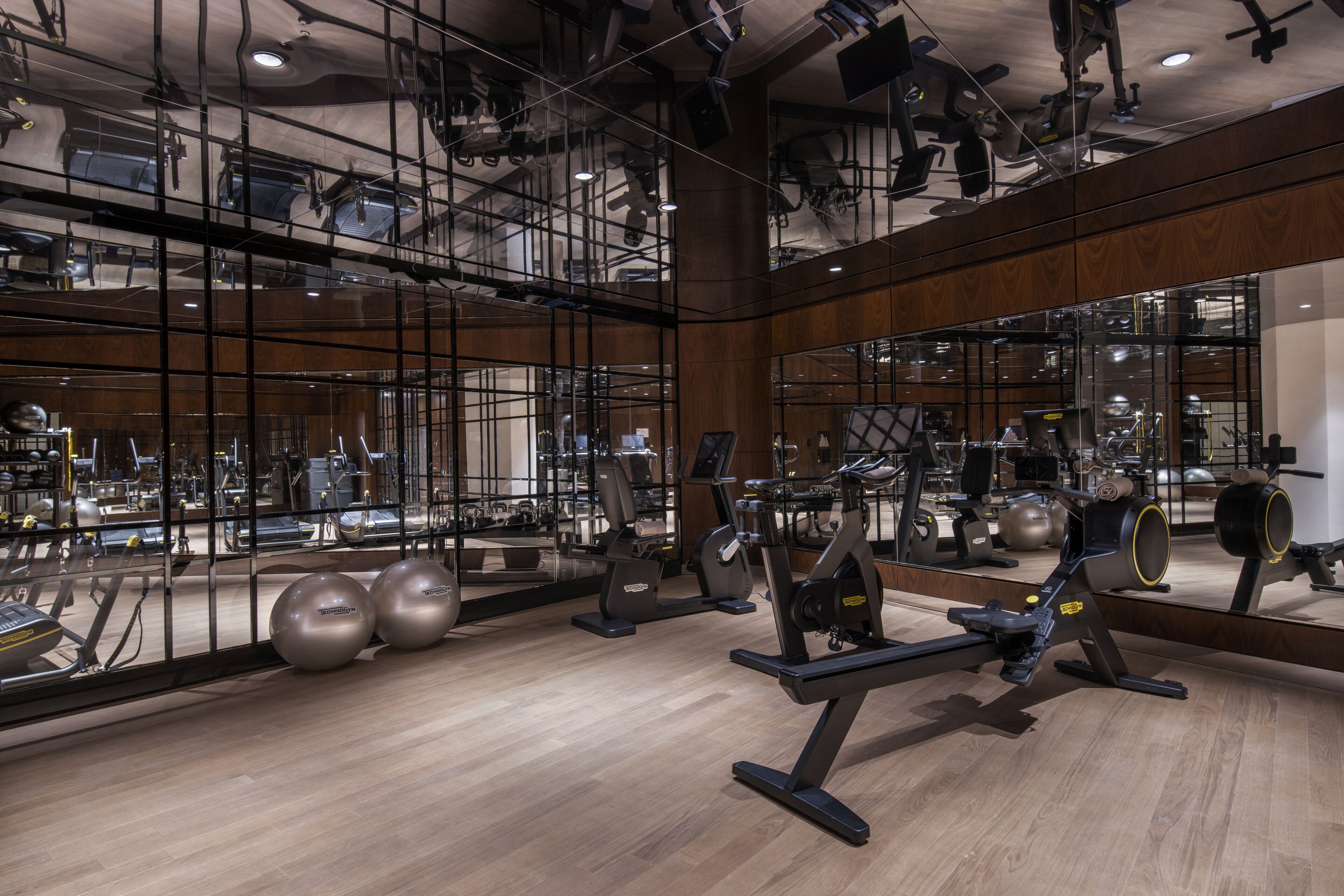 Ein modernes Fitnessstudio mit Spiegelwänden, unterschiedlichen Trainingsgeräten und Holzboden.