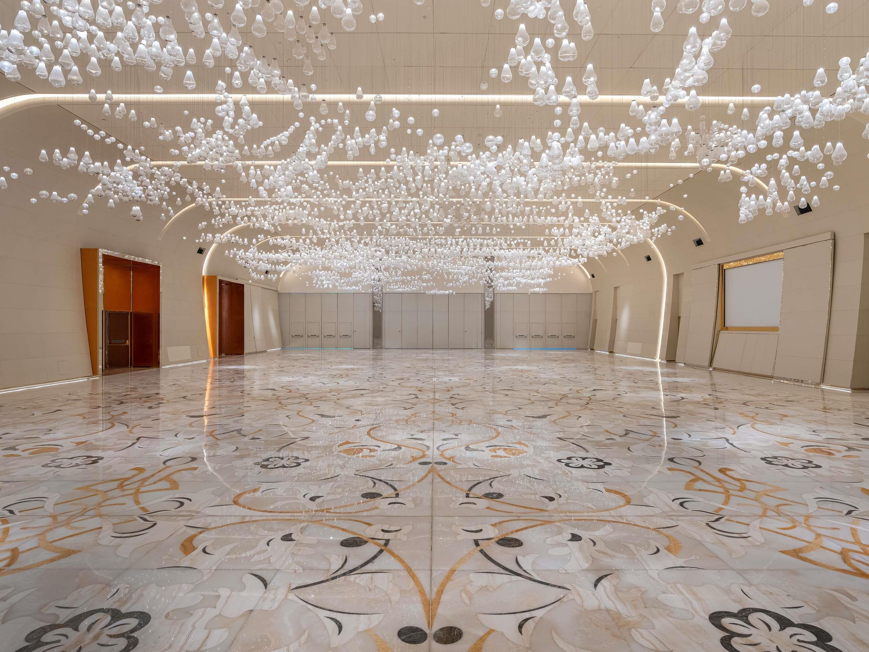 A spacious hall with a polished marble floor and a ceiling adorned with numerous hanging light fixtures.