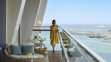 Una mujer con vestido amarillo parada en un balcón con vista al mar y al paisaje urbano.