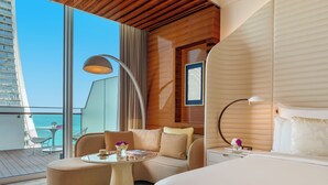 A modern hotel room with a large bed, a sofa, a small table, and a balcony with a view of the sea. - Fairmont Doha (Doha)