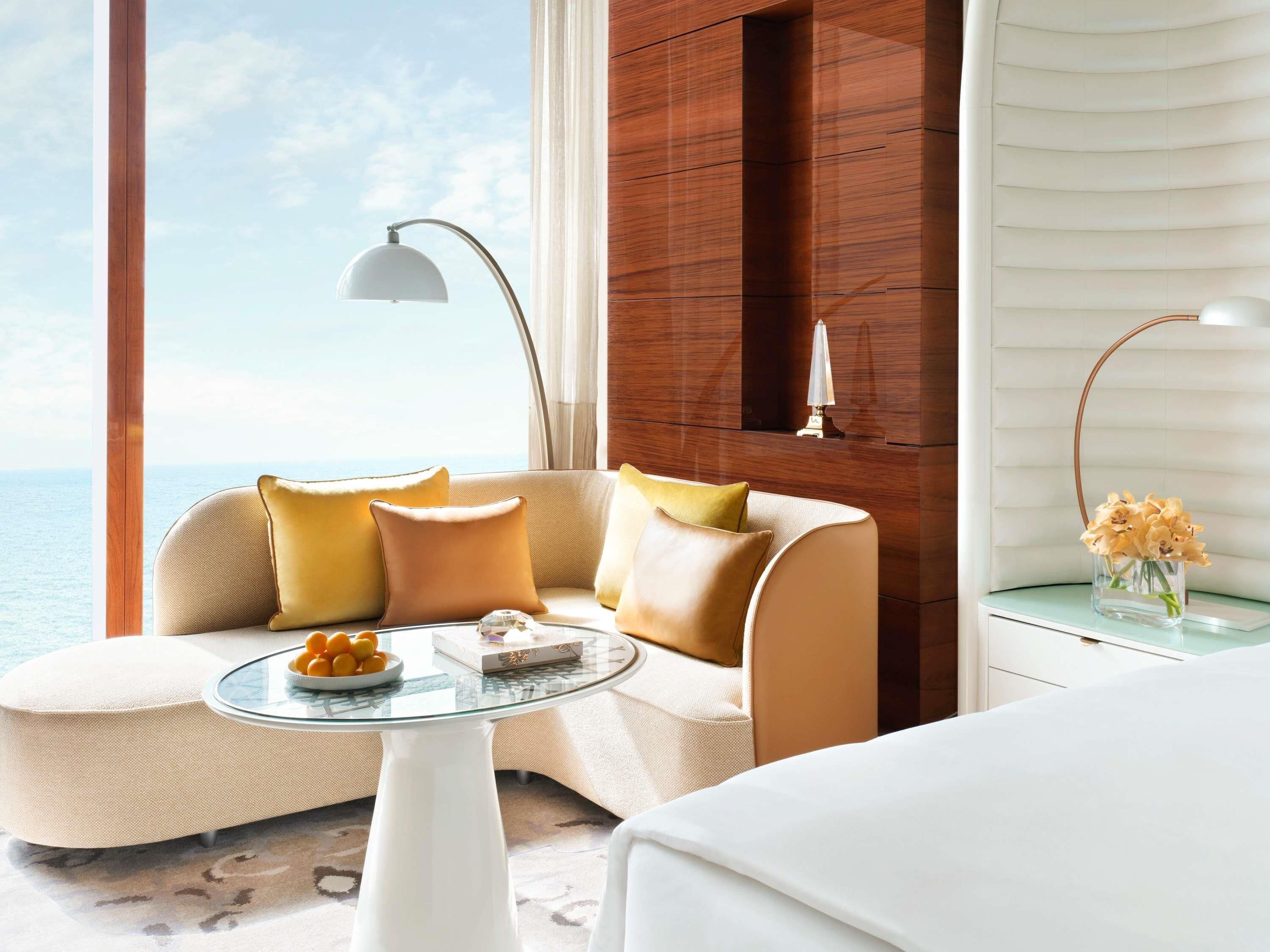 A modern room with a sofa, a glass coffee table, a lamp, and a view of the sea.