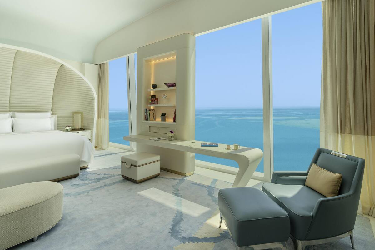 Quarto de hotel moderno com uma cama grande, uma escrivaninha, uma cadeira e vista para o mar.
