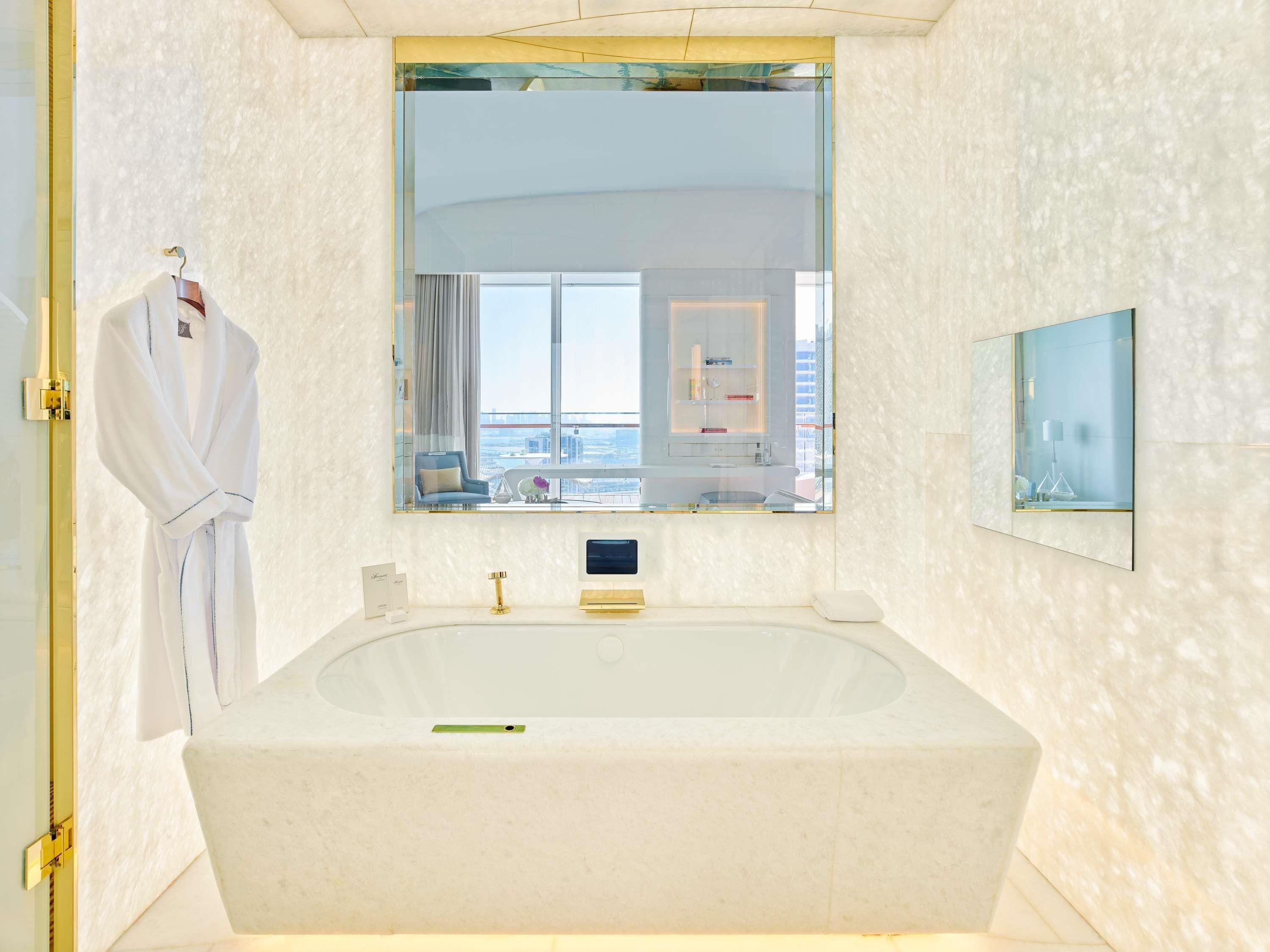A modern bathroom with a large bathtub, a vanity with a mirror, and a view of the city through the window.