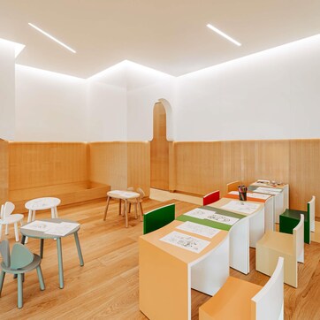 A modern, well-lit room with wooden flooring, white walls, and a long table with chairs.