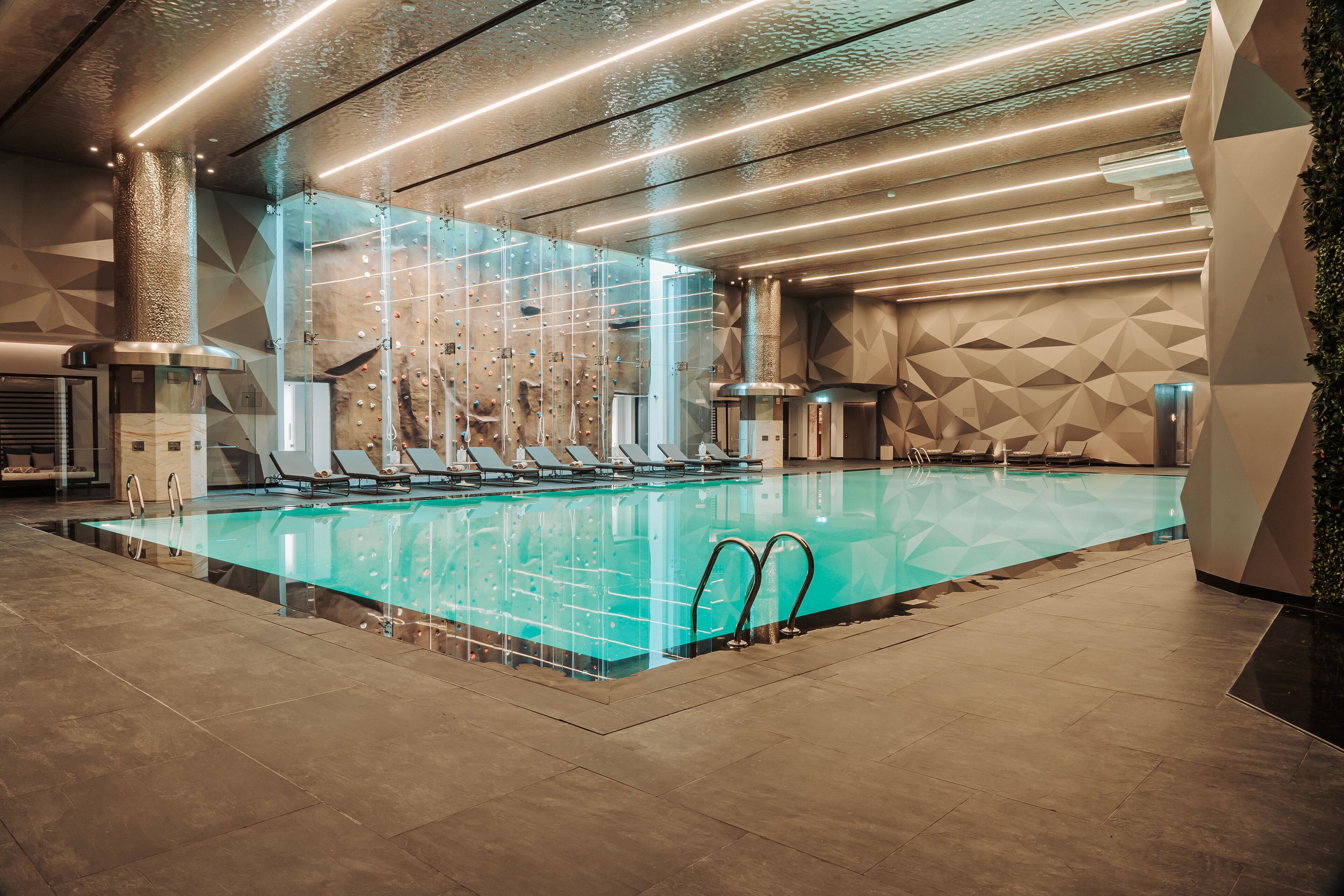 Una piscina interior moderna con paredes de vidrio transparente, múltiples carriles y un diseño geométrico en la pared.