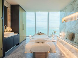 Un dormitorio moderno con una cama grande, un tocador con espejo, una mesita de noche con lámpara y vista al mar.