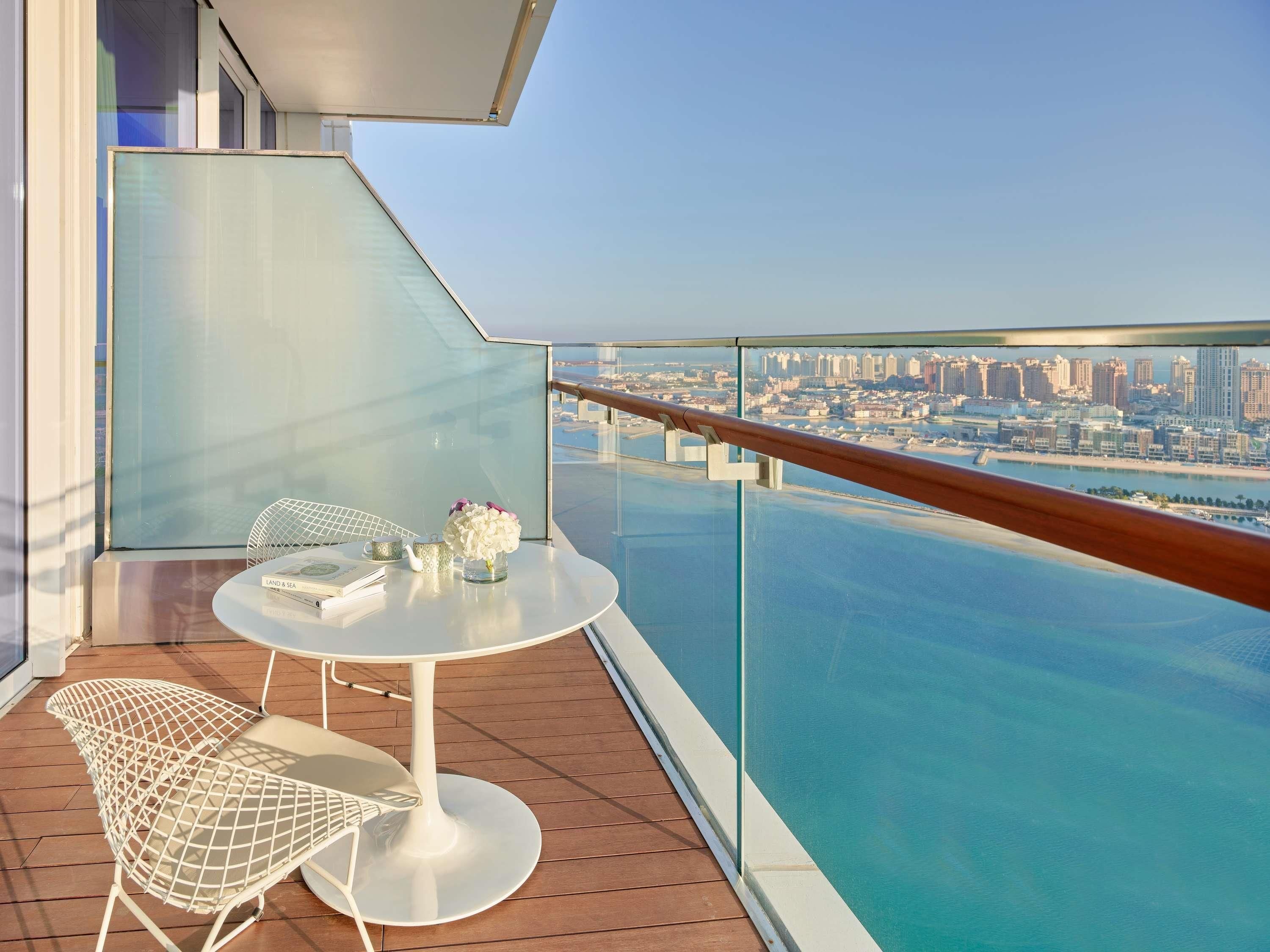 Un balcon avec une table et des chaises, donnant sur un paysage urbain et une étendue d’eau.