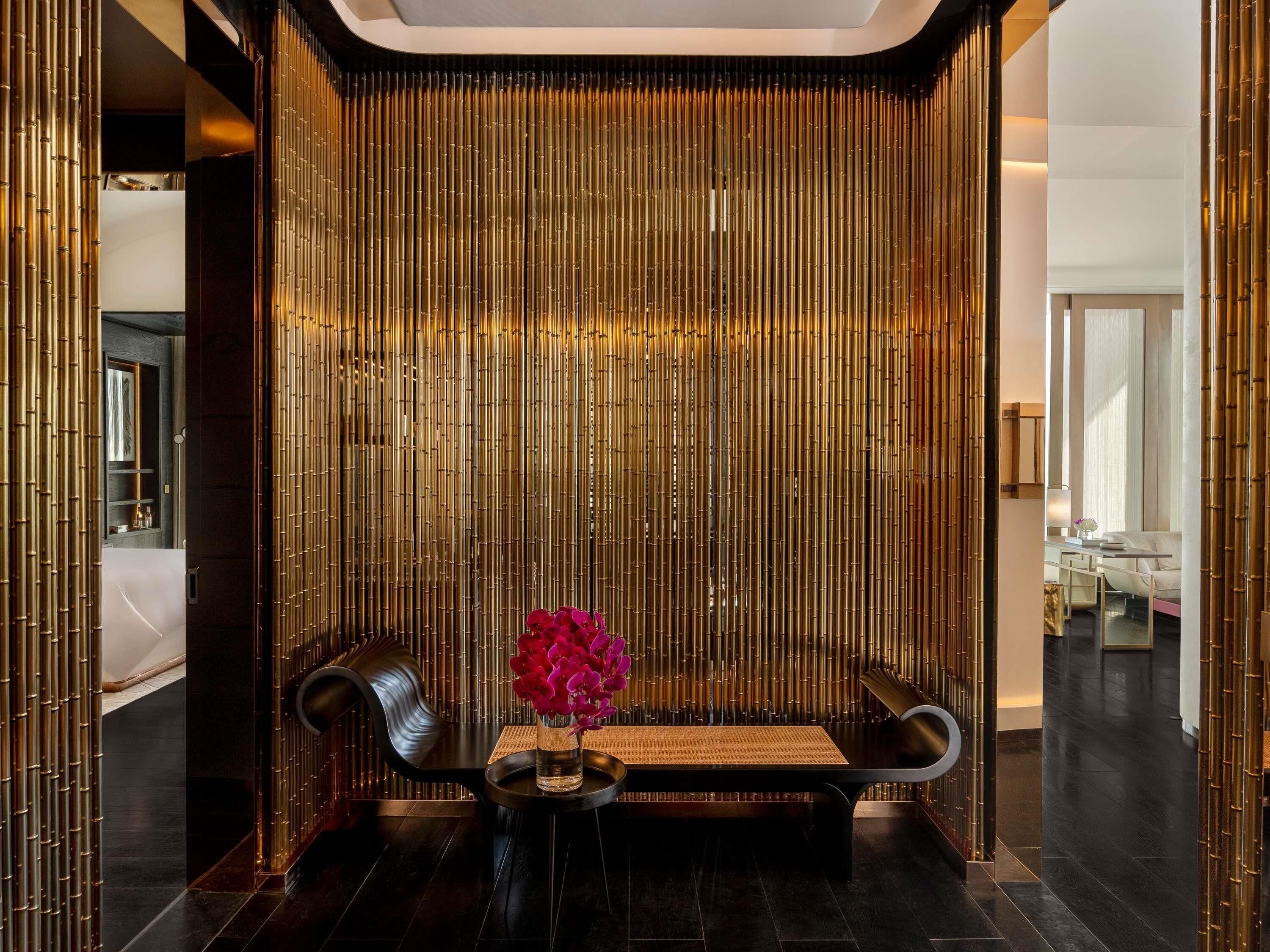 A reception area with a black sofa, a small table with a vase of flowers, and a bamboo wall.