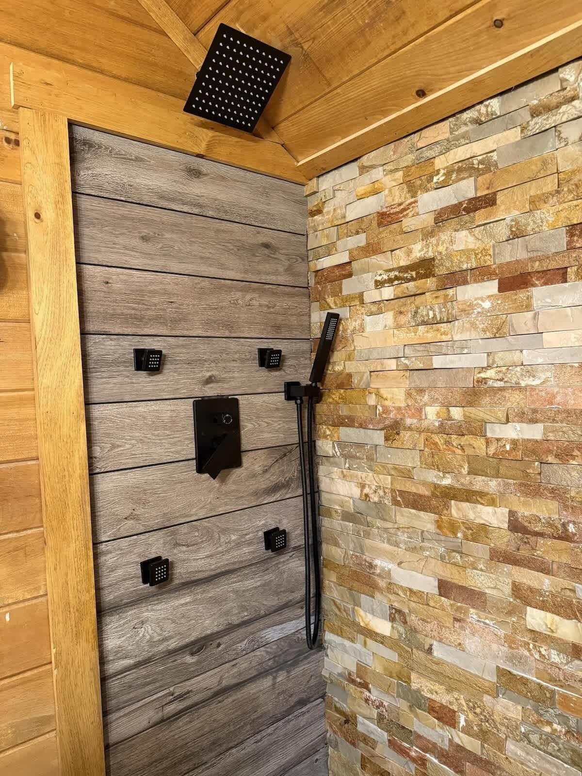 A shower area with a wooden panel wall and a stone mosaic wall.